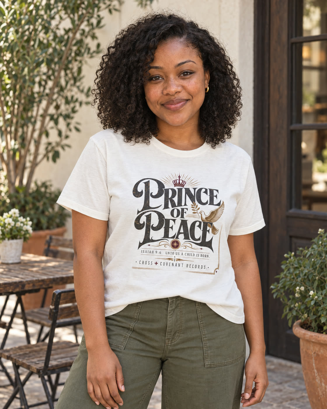 Woman with natural curls wearing the white Prince of Peace tee in a cafe courtyard